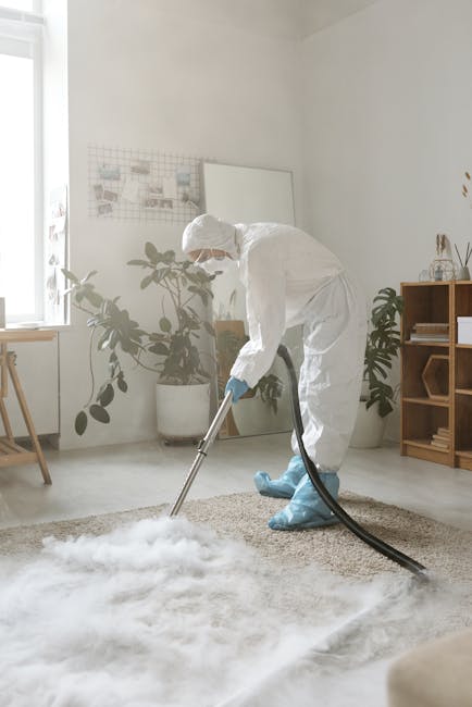 A professional cleaning technician, dressed in casual work attire, is using a flat mop with a long handle to clean a carpeted floor inside a darkened room, possibly a conference or presentation hall. 